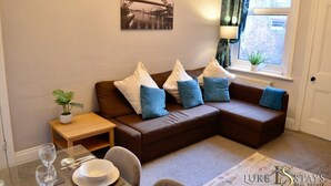 A modern living room with a brown sectional sofa, a small wooden side table, and a dining table set with plates and glasses.