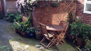 A brick wall with a wooden table and chairs, surrounded by potted plants and a wooden bench.