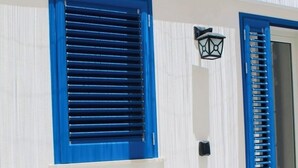A building with white walls and blue shutters, a small outdoor seating area, and a door with a black handle. - B&B Il Salento di Fioravante (Minervino di Lecce)