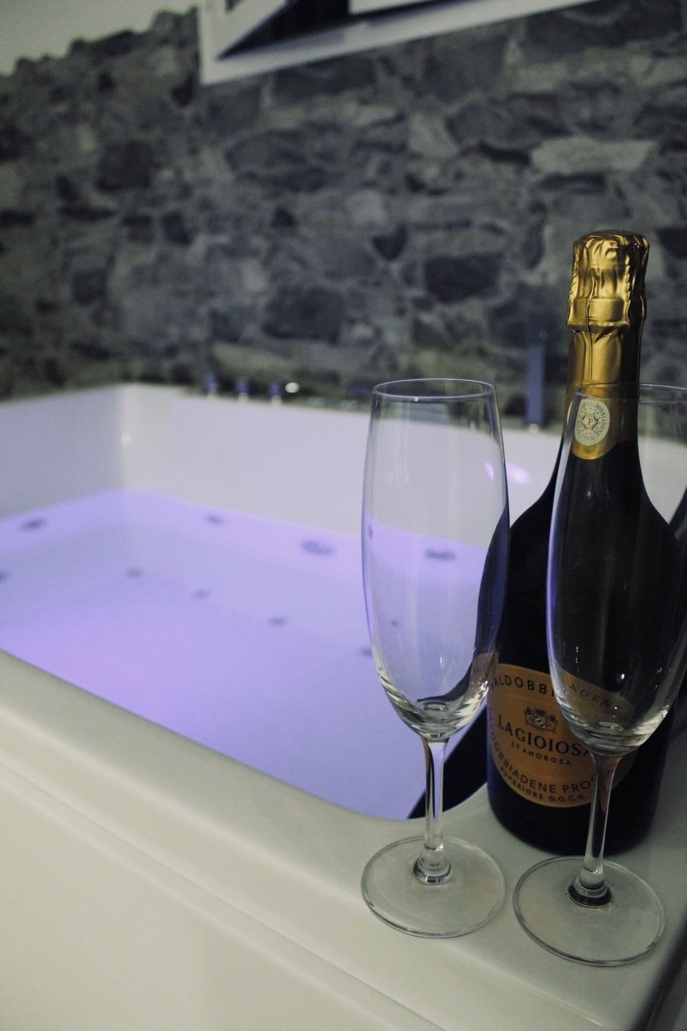 A bathtub with two wine glasses and a bottle of wine.