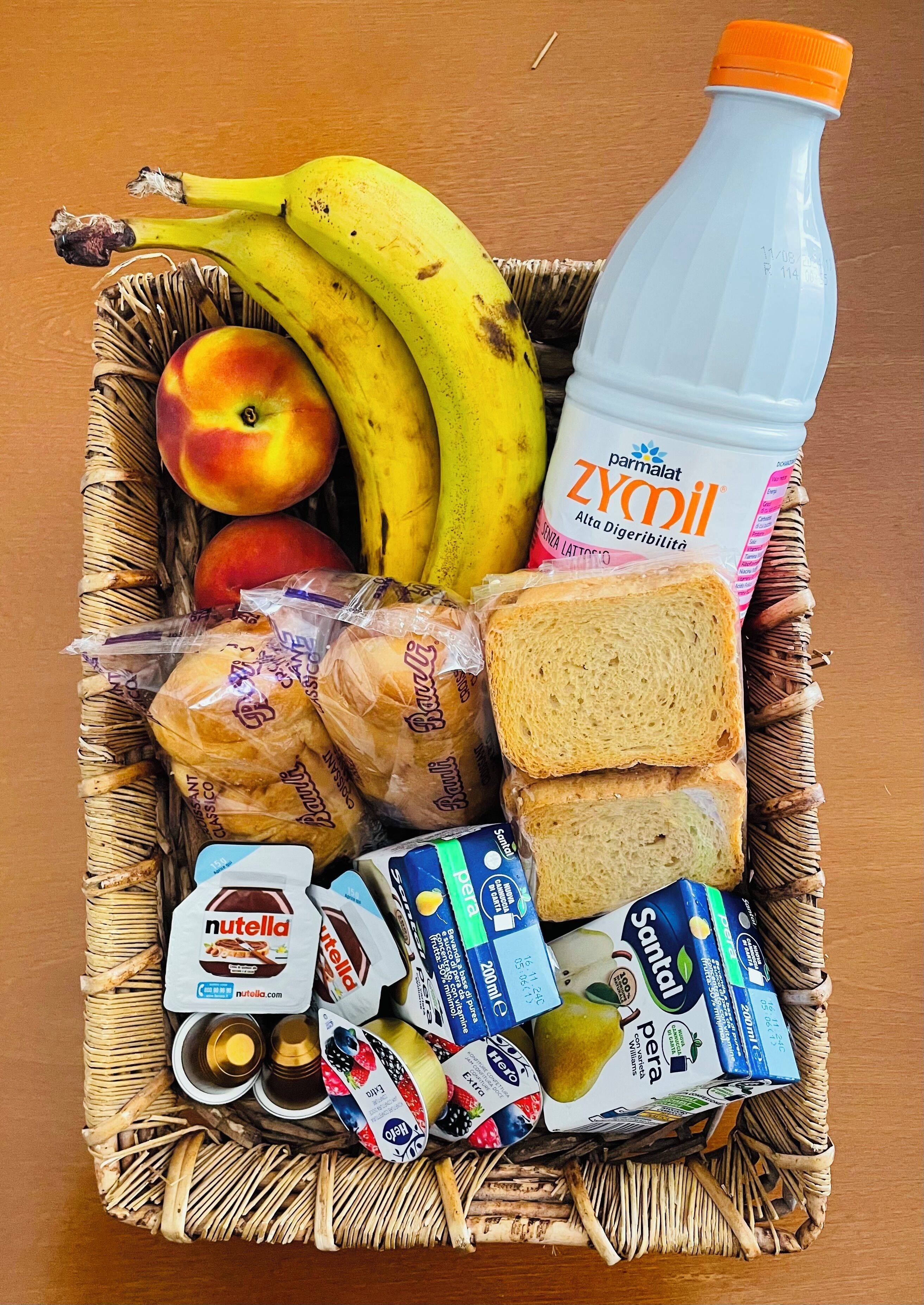 Una cesta de mimbre con frutas, pan, Nutella y leche.