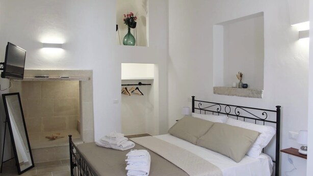 A hotel room with a bed, a television, a mirror, and a small shelf with a vase. - B&B Il Salento di Fioravante (Minervino di Lecce)