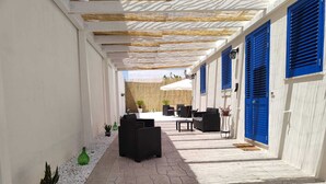 A covered outdoor area with stone flooring, black wicker furniture, and blue shutters on the walls. - B&B Il Salento di Fioravante (Minervino di Lecce)