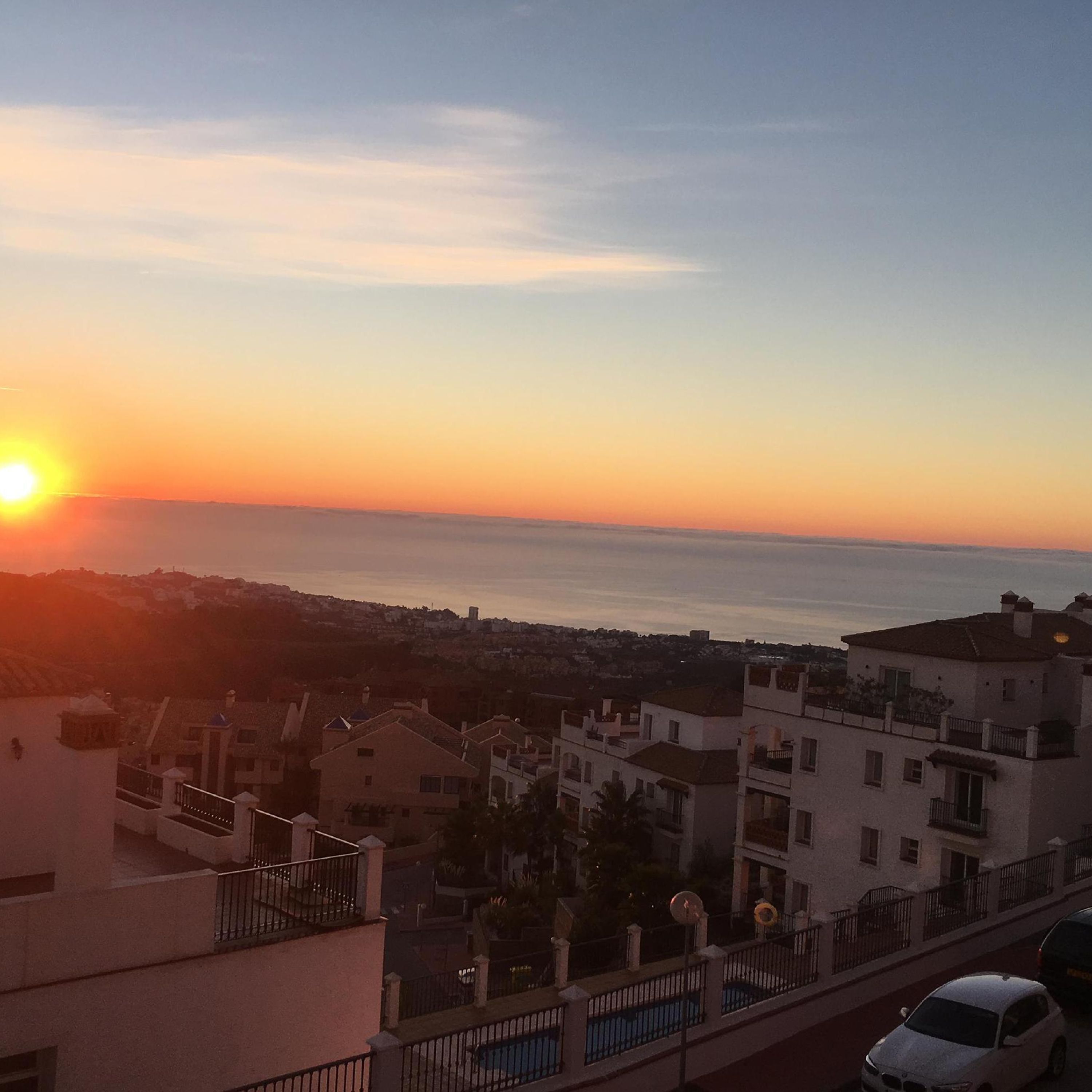 A residential area with buildings, a swimming pool, and a view of the sunset over the sea.