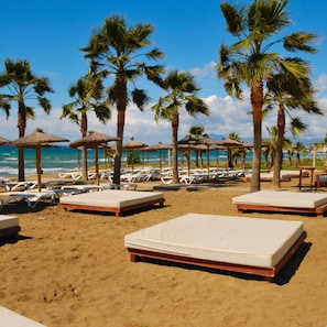 A beach with rows of sunbeds and thatched umbrellas, palm trees, and the ocean in the background. - Pool Villa Rancho Domingo Family Friendly (Benalmádena)