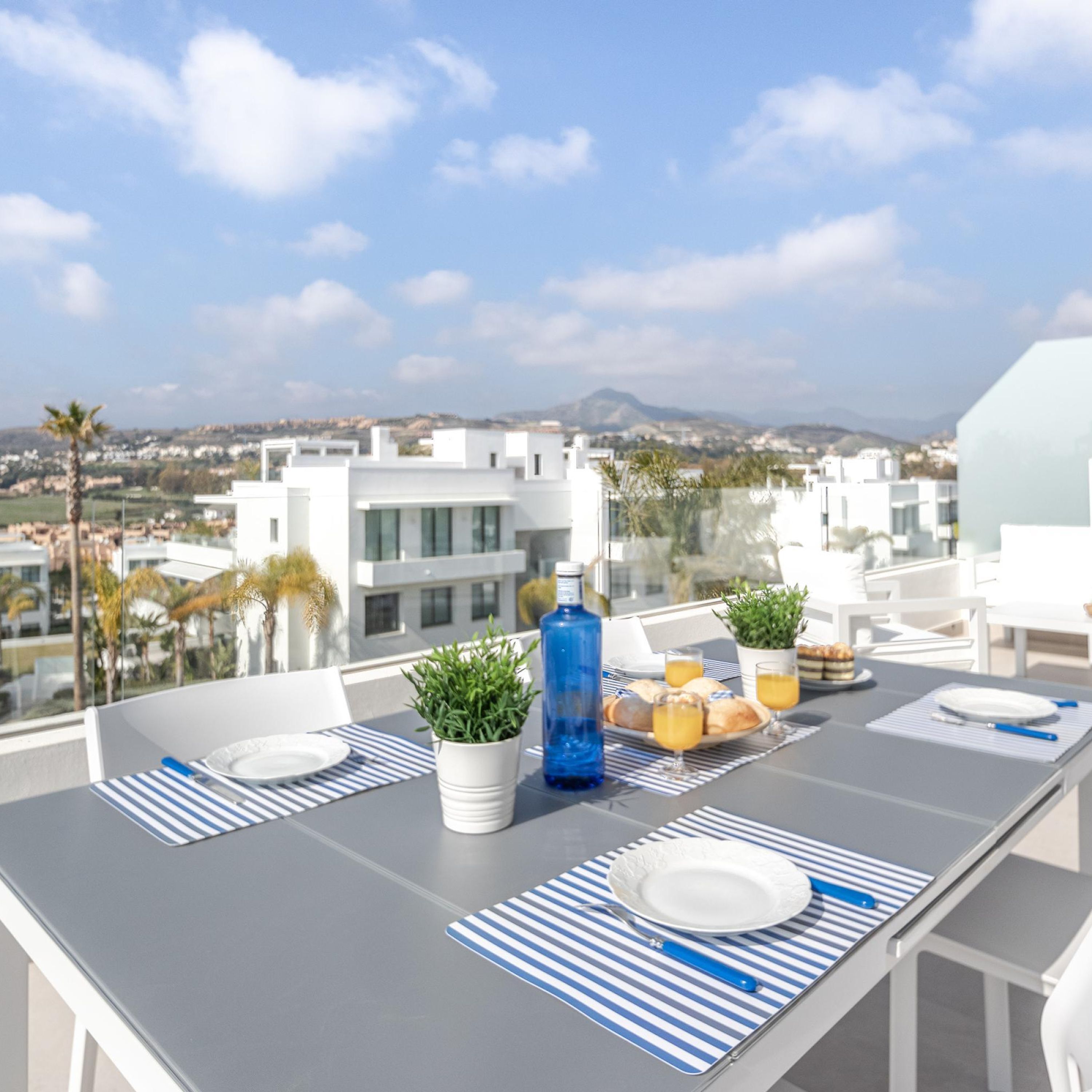 Ein Balkon mit gedecktem Tisch für das Frühstück, mit Blick auf eine Stadtlandschaft aus modernen Gebäuden und einem Berg im Hintergrund.