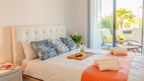 A hotel room with a large bed, a wooden tray with a bottle and glasses, and a view of the outdoor seating area. - Sunset Golf Groundfloor Shared Pool (Estepona)