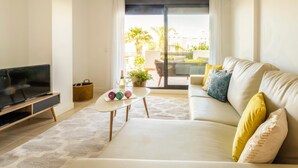 A modern living room with a sofa, a coffee table, and a TV. - Sunset Golf Groundfloor Shared Pool (Estepona)