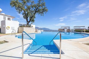 En swimmingpool med trin ned til den, omgivet af en hvid bygning og et stort træ.
