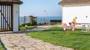 A pathway leading to a building with a thatched roof, a small fenced area, and a playground with a seesaw and a swing set. - Mi Capricho Beach Front sea View Pool (Mijas)