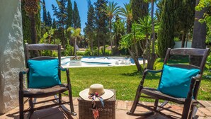 Two rocking chairs with teal cushions and a wicker basket with a hat and scarf on a patio with a pool and greenery in the background. - Pool Villa Jazmin in Marbella (Estepona)