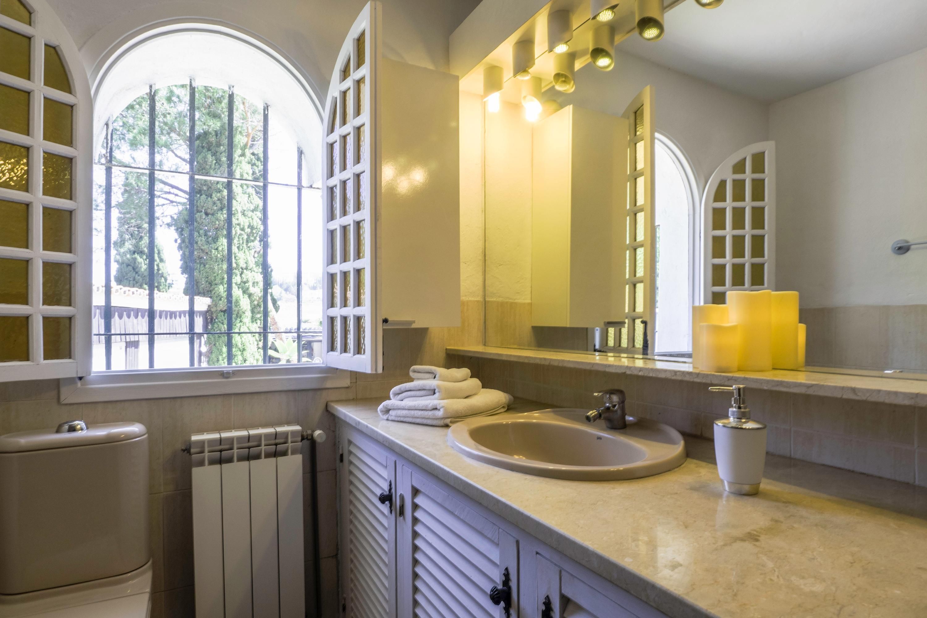 Une salle de bain avec une grande fenêtre, un lavabo, un miroir et des toilettes.