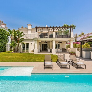 Une maison à deux étages avec une piscine, un espace salon extérieur et une pergola.