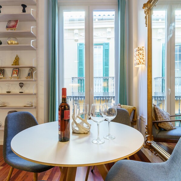 A round table with a bottle and two glasses, a blue chair, a sofa with cushions, a decorative mirror, and a shelf with various items. - M Laga Center Old Town (Málaga)