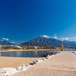 Une promenade en bord de mer, avec un monument en pierre, une plage et une montagne en arrière-plan.