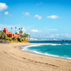 A beach with a red building, palm trees, and a view of the sea and distant boats. - Sunny Tranquility With Pool (Benalmádena)