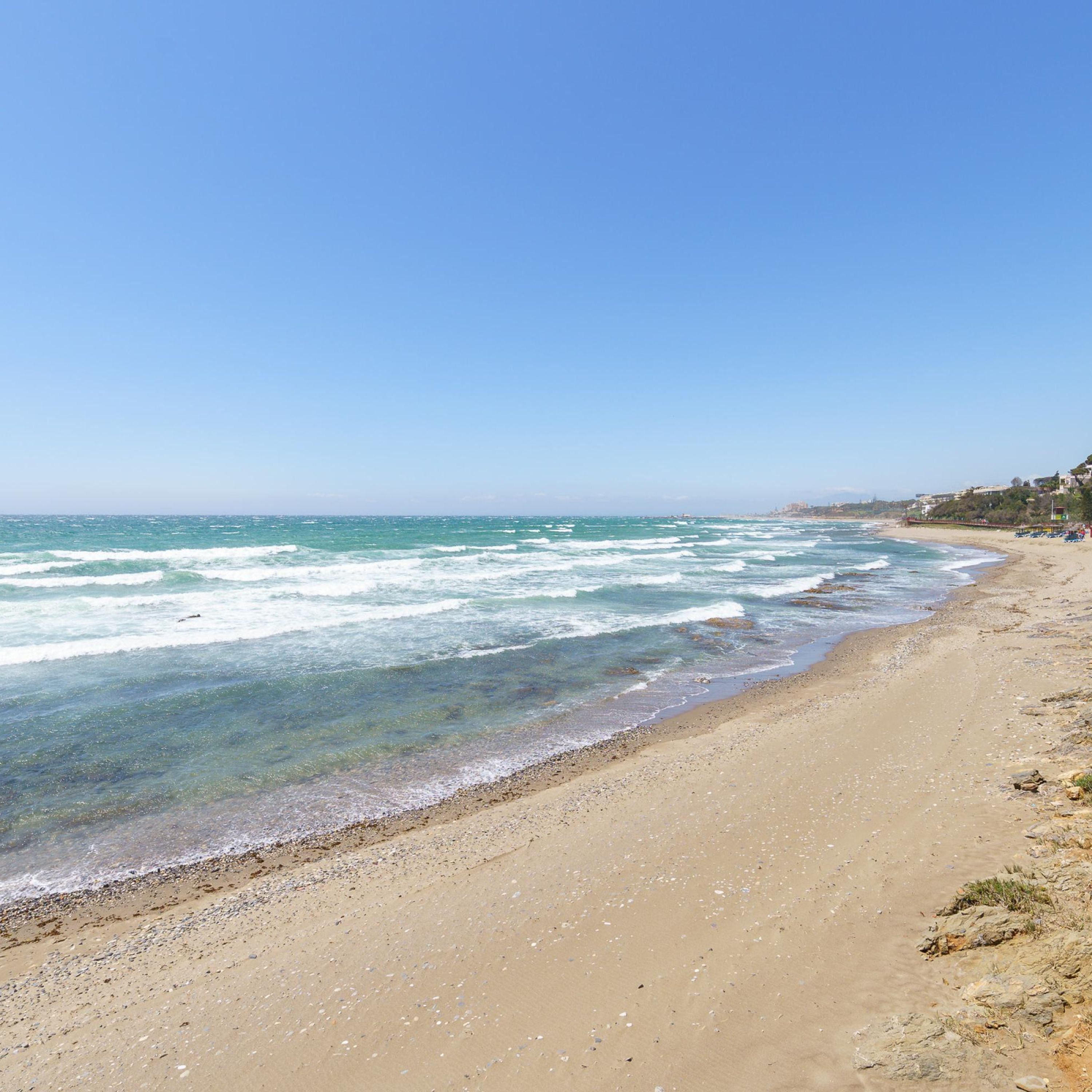 A sandy beach with clear blue water and a clear sky.