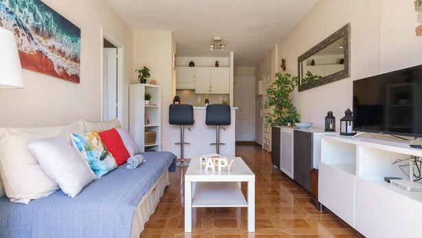 A modern living room with a sofa, a coffee table, a TV, and a kitchen area with cabinets and a dining table. - Sunny Zoco Calahonda (Mijas)