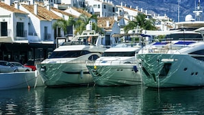 Ένα λιμάνι με πολυτελή σκάφη αγκυροβολημένα, λευκά κτίρια με κόκκινες κεραμοσκεπές και βουνά στο βάθος.