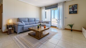 A modern living room with a grey sofa, a wooden coffee table, and a large window with curtains. - Sunset Seaview Corner With Pool (Estepona)