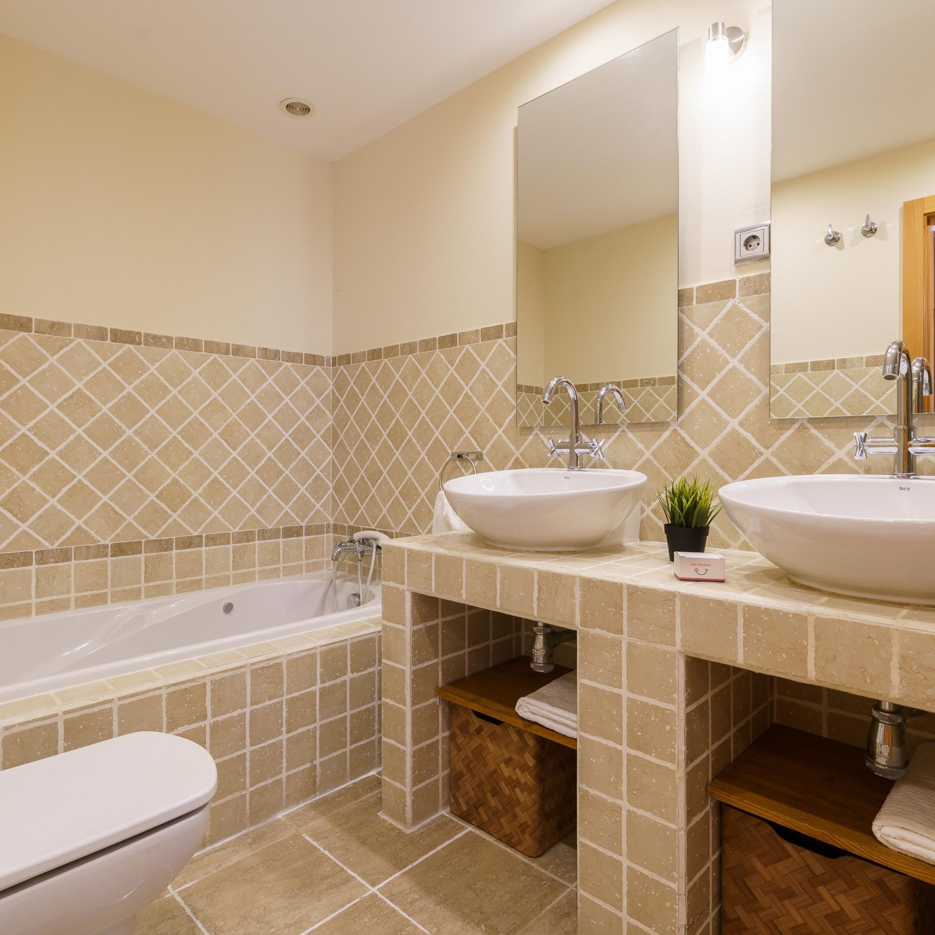 Ein Badezimmer mit einer Badewanne, zwei Waschbecken, einem Spiegel und einer Toilette.