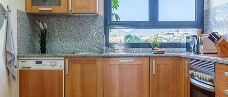 A kitchen with wooden cabinets, a built-in dishwasher, a window with a view, and a countertop with a knife block and wine glasses.