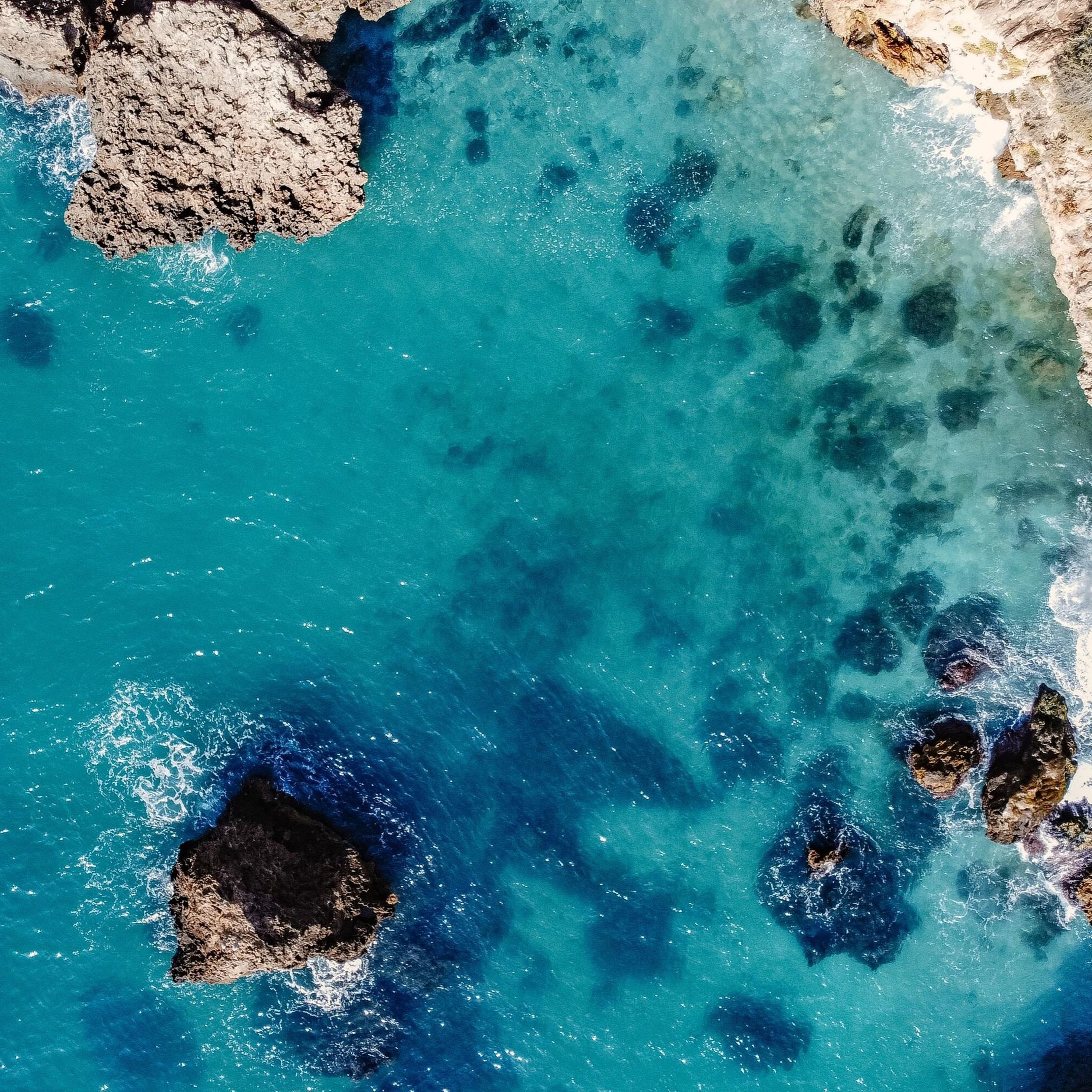 A coastal area with clear turquoise waters, rocky formations, and a rugged coastline.