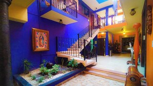 Ein mehrgeschossiges Interieur mit einer Treppe, einem gerahmten religiösen Gemälde und einer kleinen Gartenanlage.
