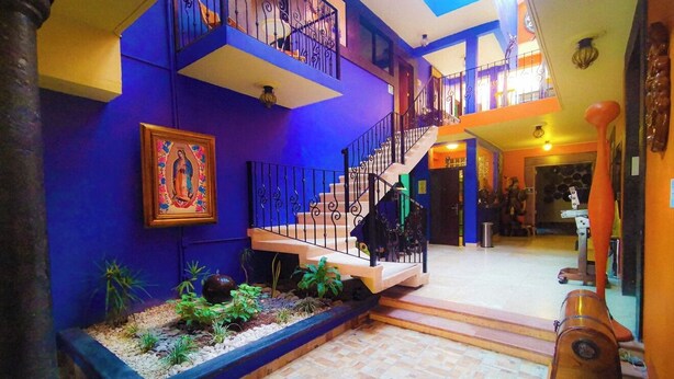 Un interior de varios niveles con una escalera, un cuadro religioso enmarco y una pequeña zona ajardinada.