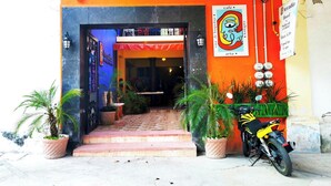 Fachada de edificio con colores rojo y negro, una motocicleta estacionada afuera y plantas en macetas en la entrada.