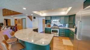 Een moderne keuken met een marmeren eiland, groene kasten, roestvrijstalen apparatuur en een houten plafond.