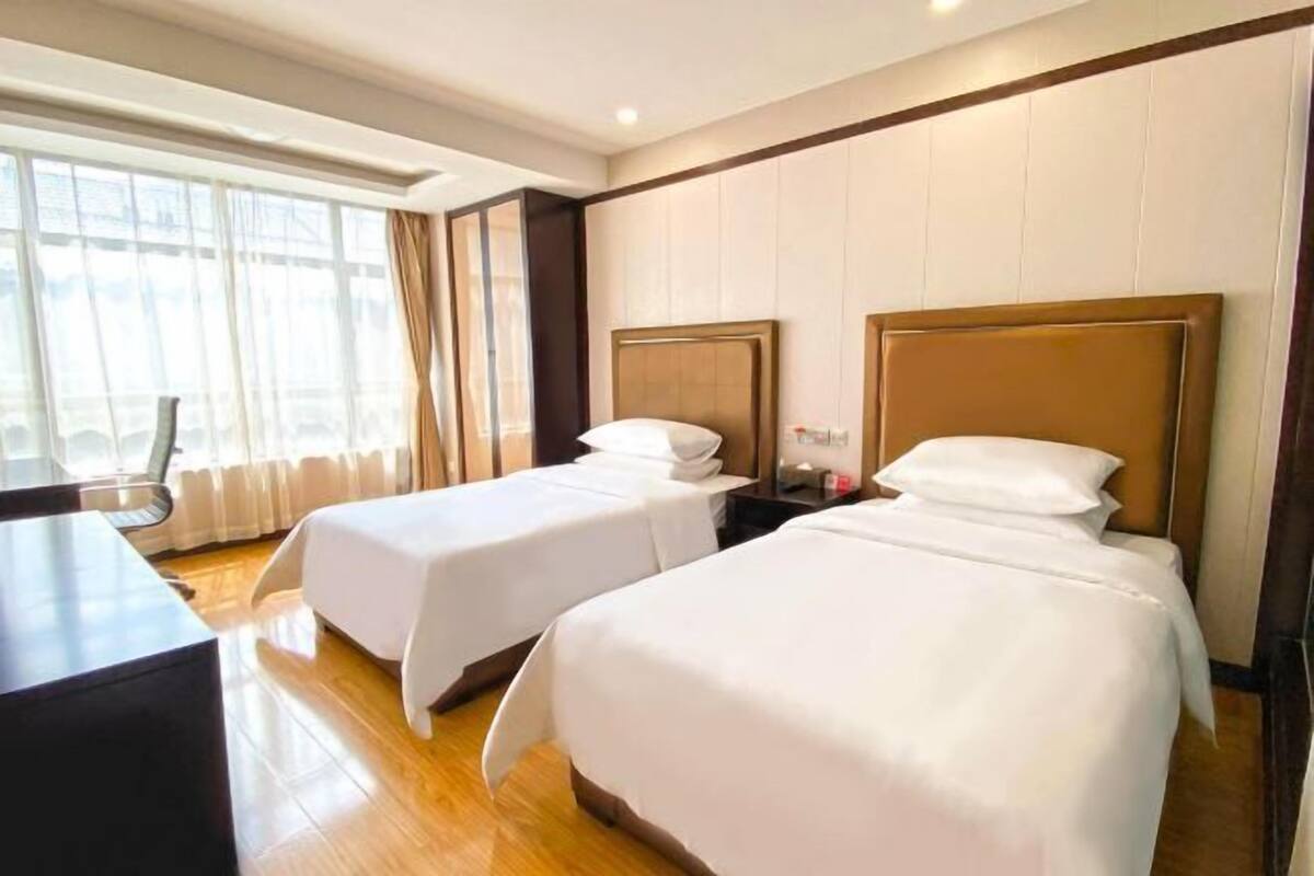 A hotel room with two beds, a desk, and a large window with curtains.