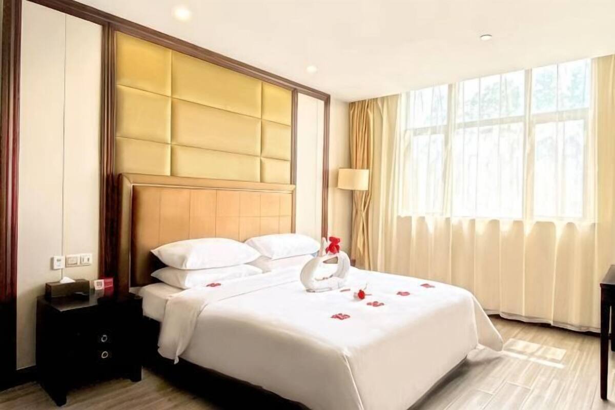 A hotel room with a large bed, a nightstand, a lamp, and a window with curtains.