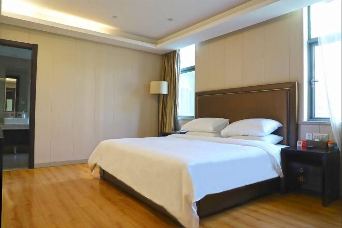 A hotel room with a large bed, a bedside table, a lamp, and a window.