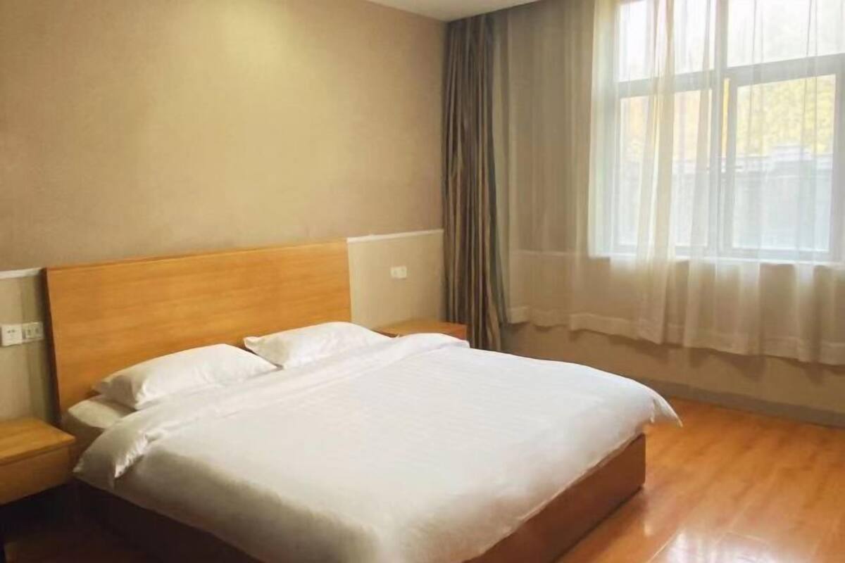 A single bed with a wooden headboard in a room with a window and curtains.