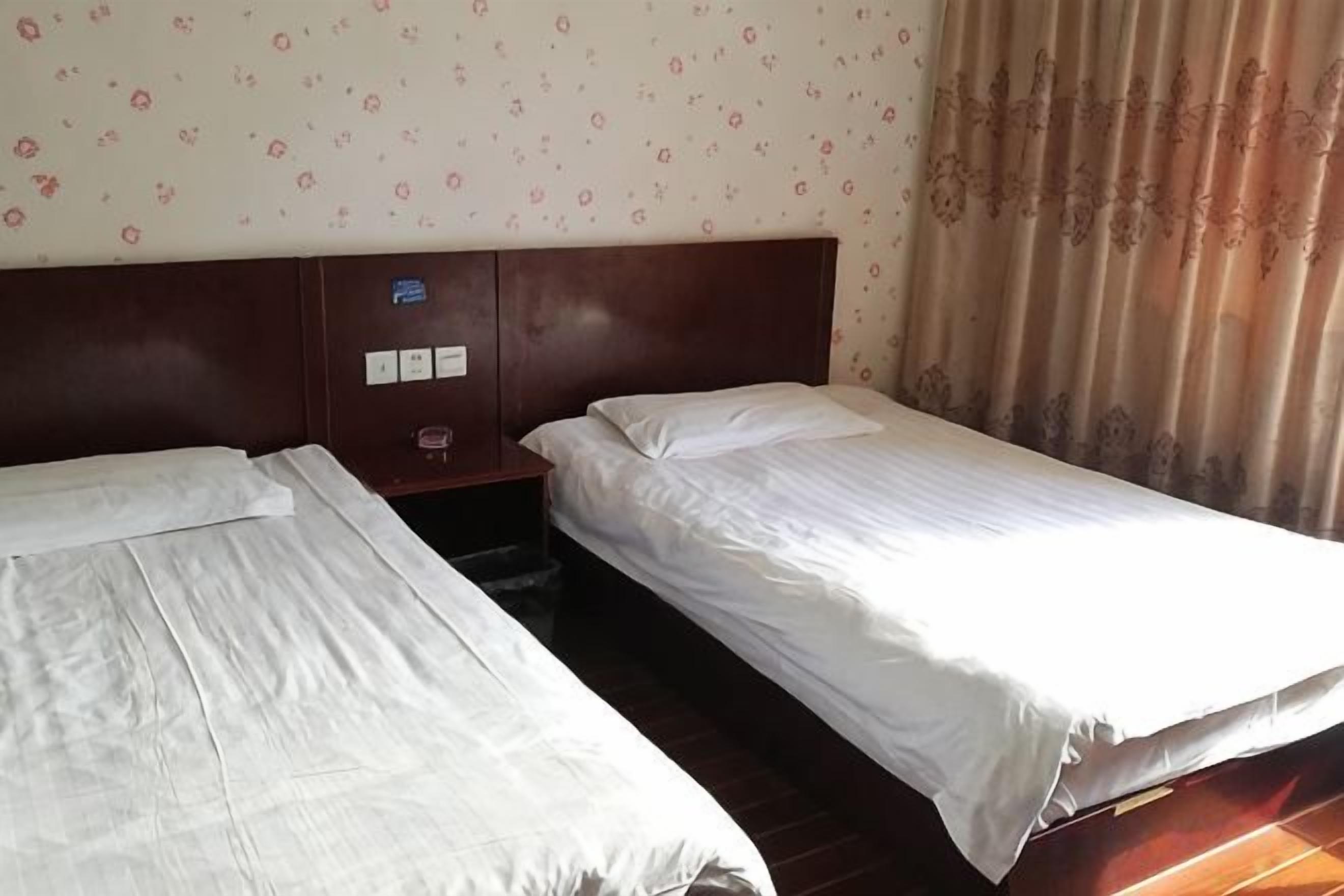 A hotel room with two single beds, a wooden headboard, a small nightstand, and a patterned wallpaper.