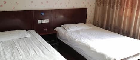 A hotel room with two single beds, a wooden headboard, a small nightstand, and a patterned wallpaper.