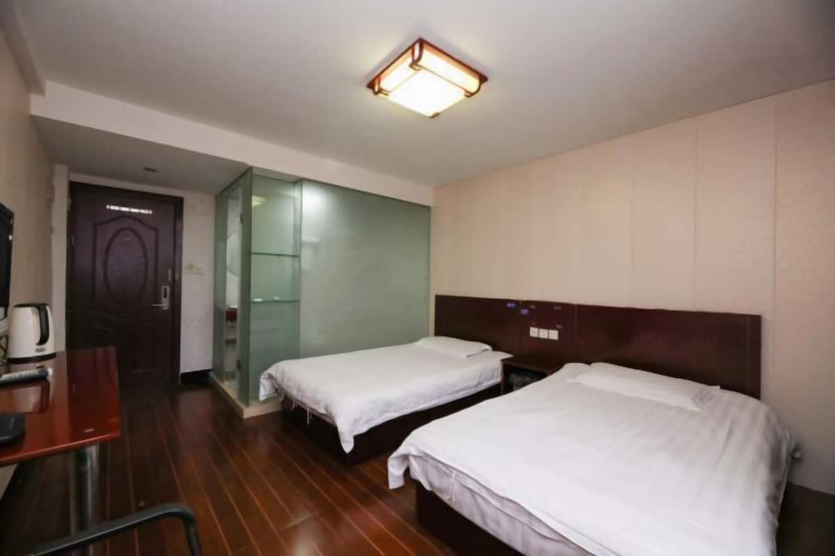 A hotel room with two single beds, a wooden desk, a chair, a coffee maker, and a glass partition wall.