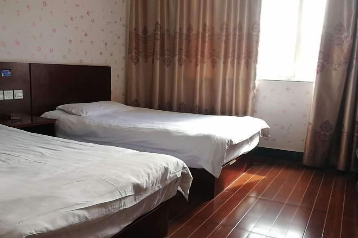 A hotel room with two single beds, wooden flooring, floral wallpaper, and a window with curtains.
