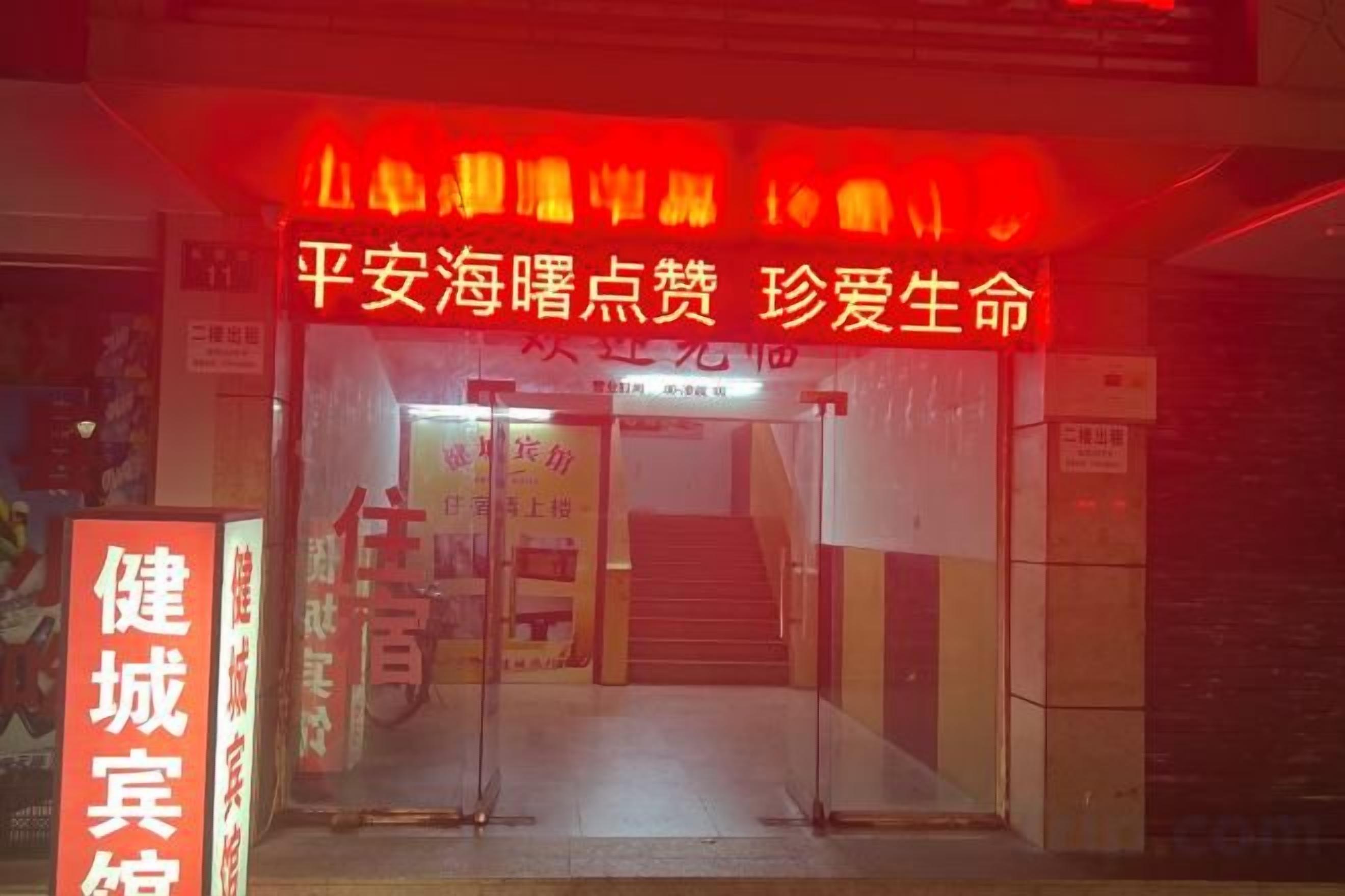 A building entrance with a staircase leading up to a door. There is a sign with Chinese characters and a red neon sign above the door.