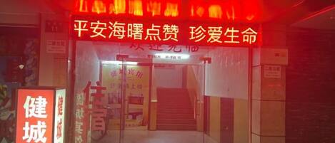 A building entrance with a staircase leading up to a door. There is a sign with Chinese characters and a red neon sign above the door.