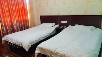 Dos camas individuales con cabeceras, una mesita de noche con lámpara y una ventana con cortinas rojas.
