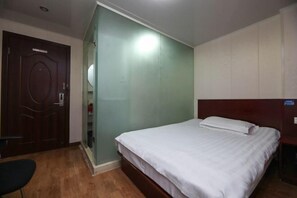 Ett hotellrum med en säng, en trädörr, en stol och en vägg med en lampa.