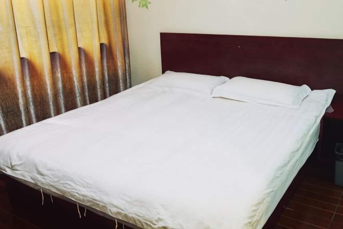 A bed with white bedding, a dark headboard, and a curtain with vertical slats.