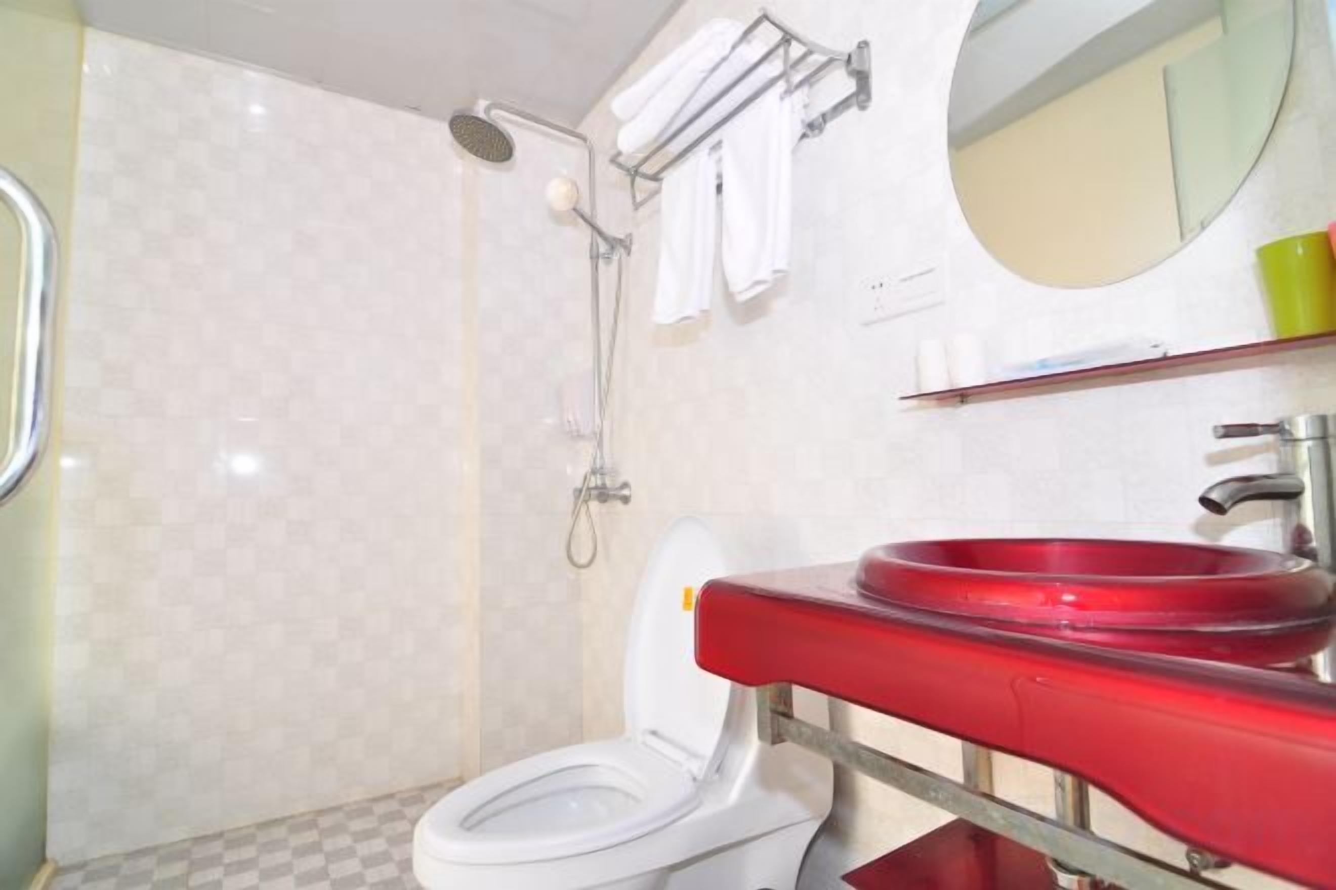 A bathroom with a white toilet, a red sink, and a shower area.