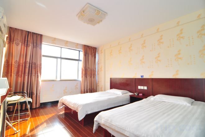 A hotel room with two beds, a desk, and a window with curtains.