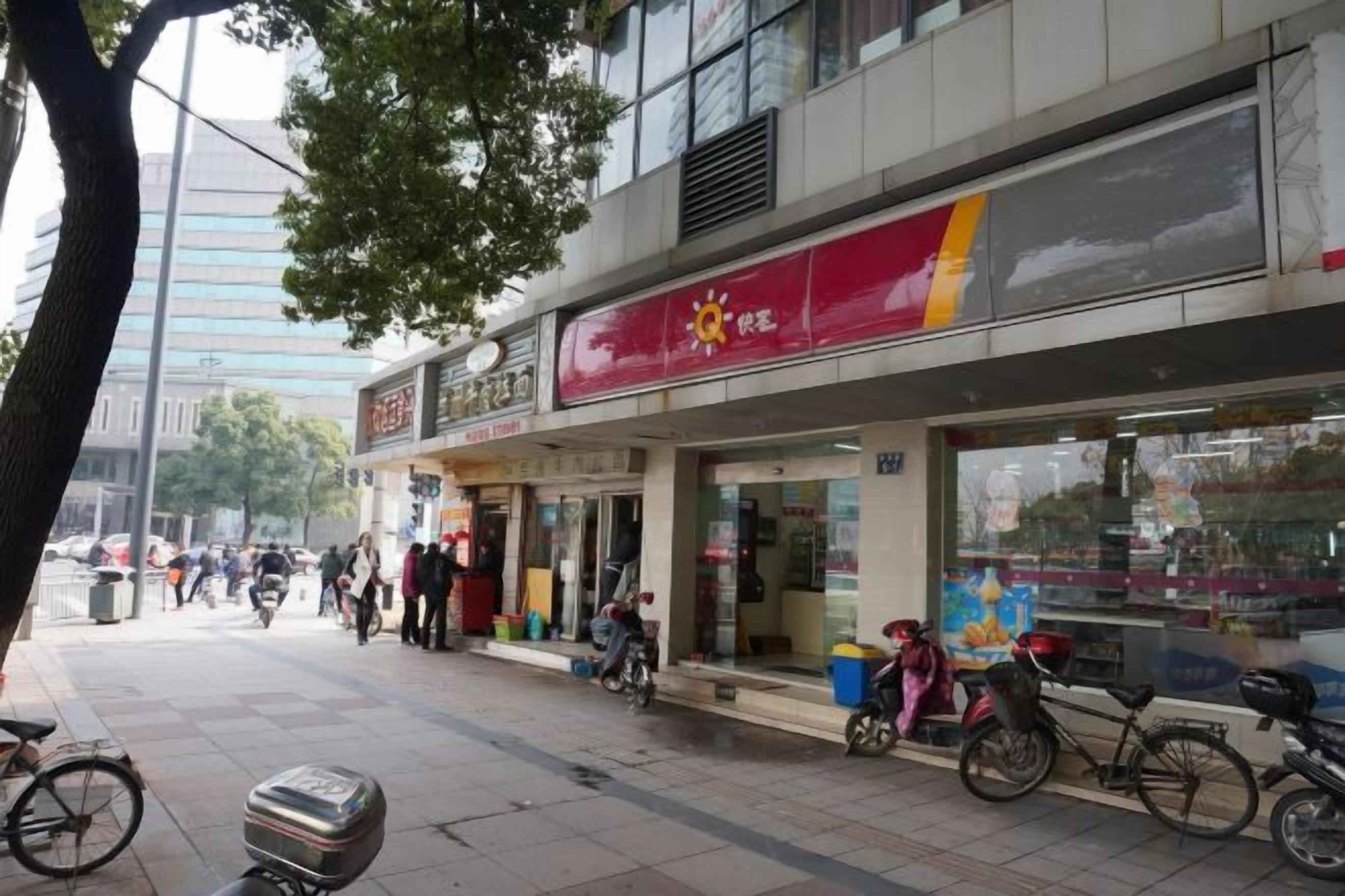 A street with a row of shops, including a pharmacy and a restaurant with outdoor seating.