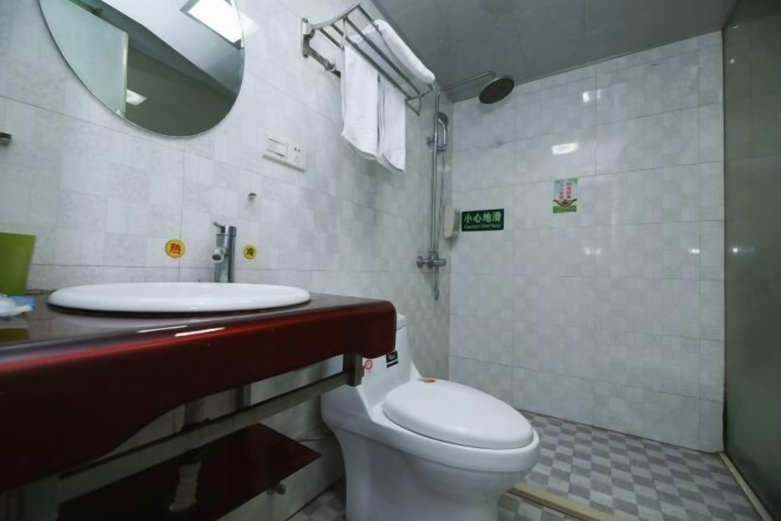 Un baño con inodoro blanco, un lavabo con encimera roja, un espejo y una zona de ducha.