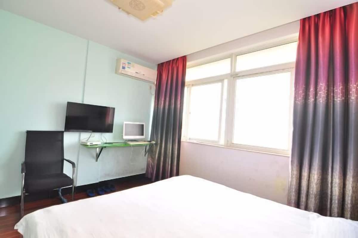 A hotel room with a bed, a desk with a computer, a TV, and a window with curtains.