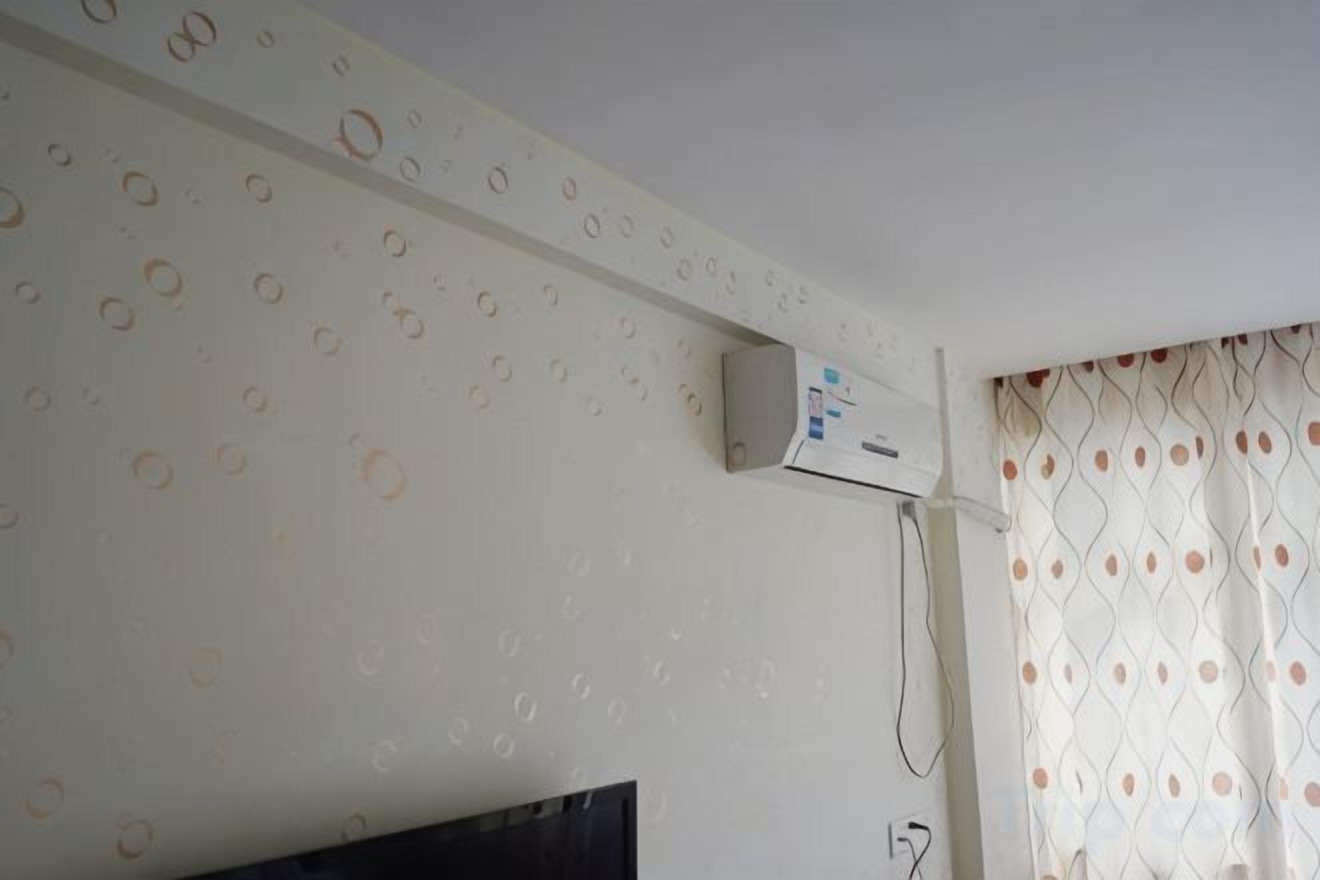 Une pièce avec un mur décoré de motifs, un téléviseur à écran plat et une fenêtre avec des rideaux.
